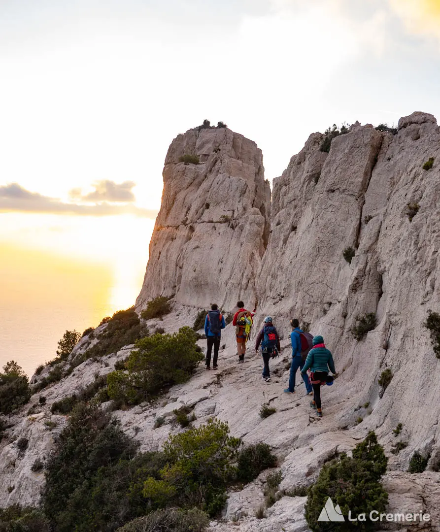 Cinq personnes marchent sous le rocher des Goudes devant un coucher de soleil