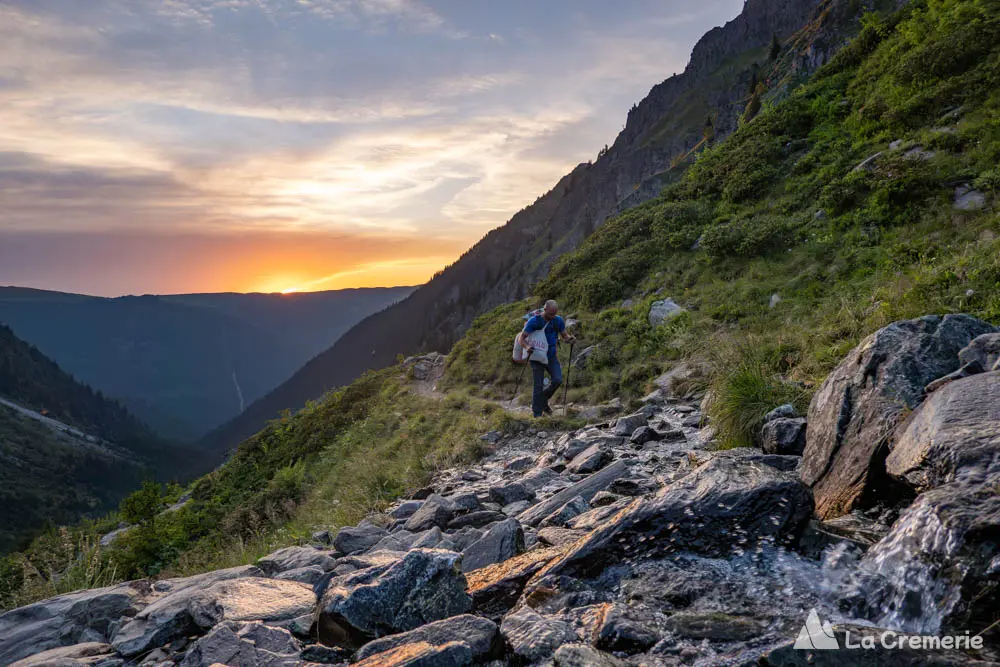 Une personne marche sur un sentier de Belledonne dans la Combe Madame avec le couché du soleil